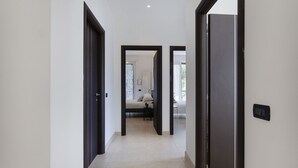 A corridor with dark wooden doors leading to a room with a bed, a chair, and a window.