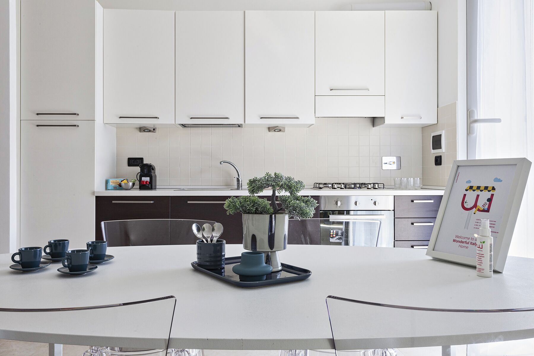 A modern kitchen with white cabinets, a coffee machine, and a small potted plant on the counter.