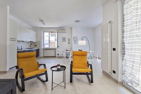 A modern apartment with two yellow armchairs, a small table, a kitchen, and a dining area. - Shelley Apartments By Wonderful Italy (Genoa)