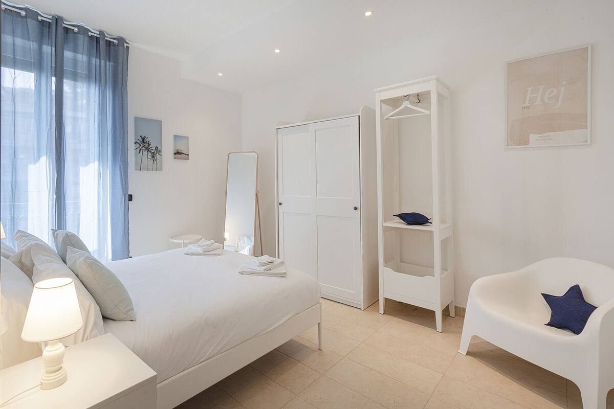 A bedroom with a bed, a wardrobe, a chair, and a bedside table with a lamp.