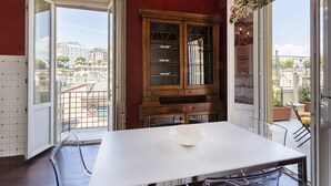 A dining area with a white table and chairs, a wooden cabinet with glass doors, and a view of the city through open doors. - The Liberty Rooftop Terrace By Wonderful Italy (Genoa)