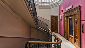 A grand staircase with ornate black railings and wooden handrails, leading to a room with a large window and a pink wall. - The Liberty Rooftop Terrace By Wonderful Italy (Genoa)