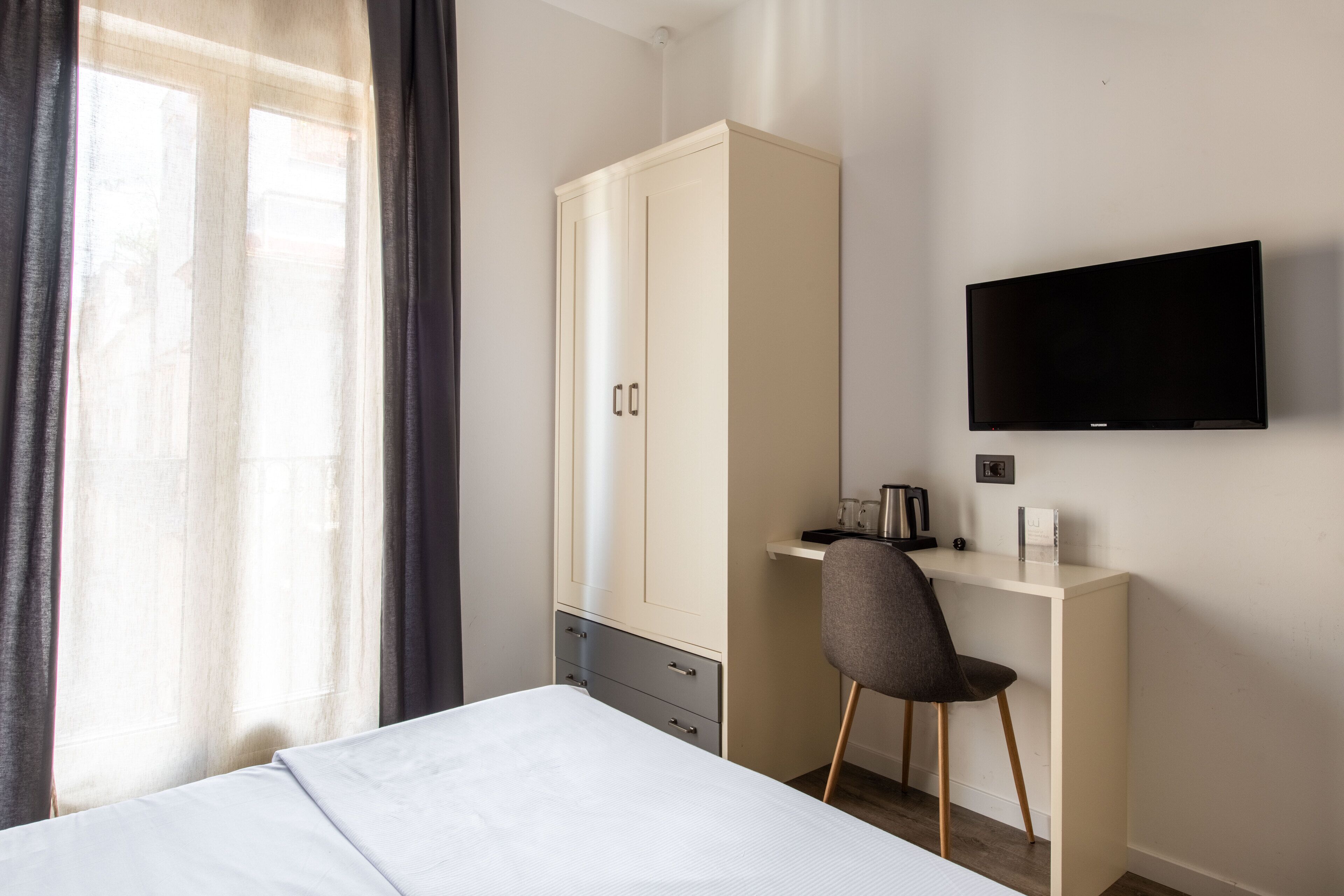 Une chambre d’hôtel comprenant un lit, un bureau avec une chaise, une armoire et un téléviseur fixé au mur.