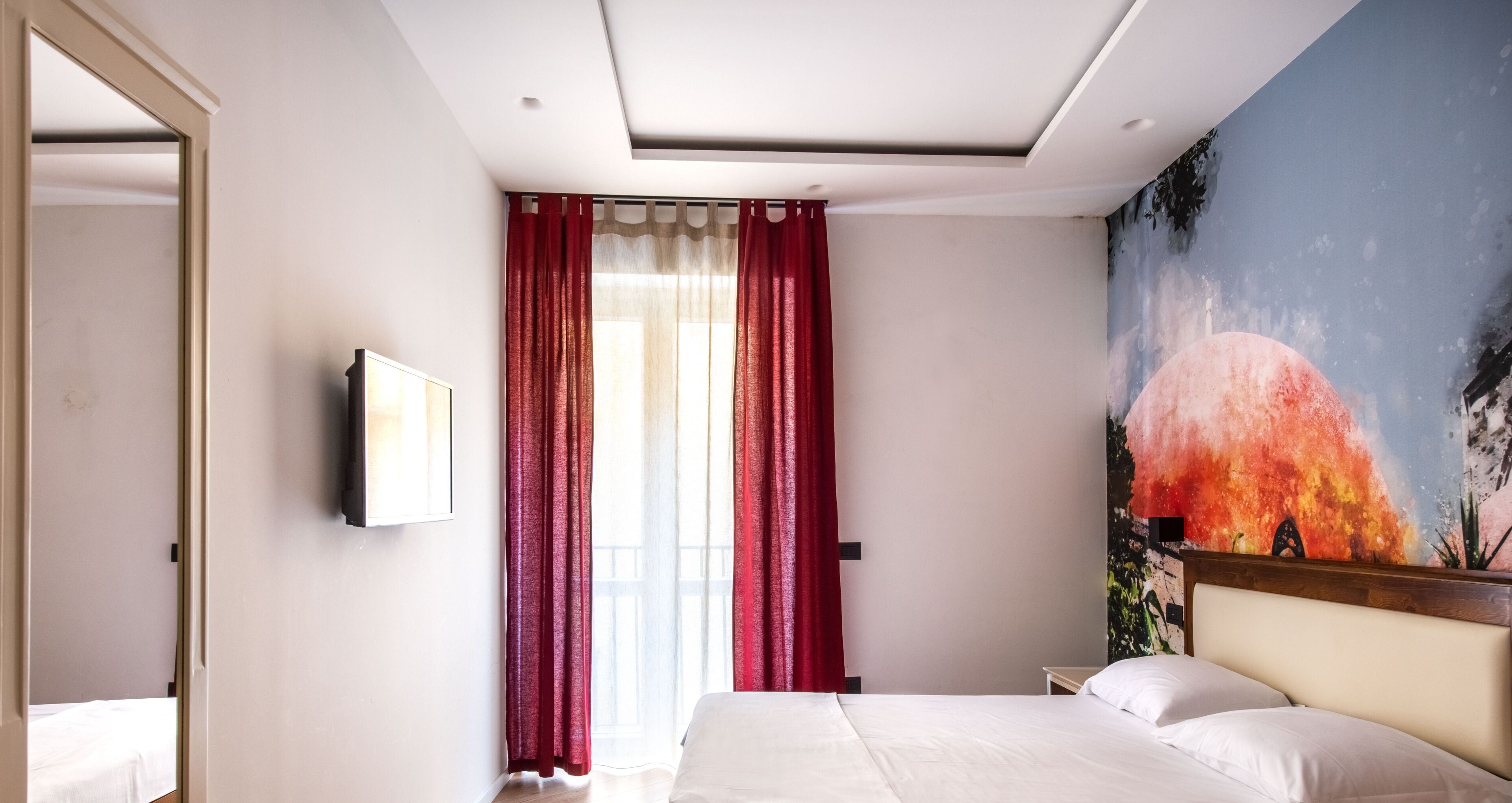 Ein Hotelzimmer mit einem Bett, einem Gemälde und einem Fenster mit roten Vorhängen.