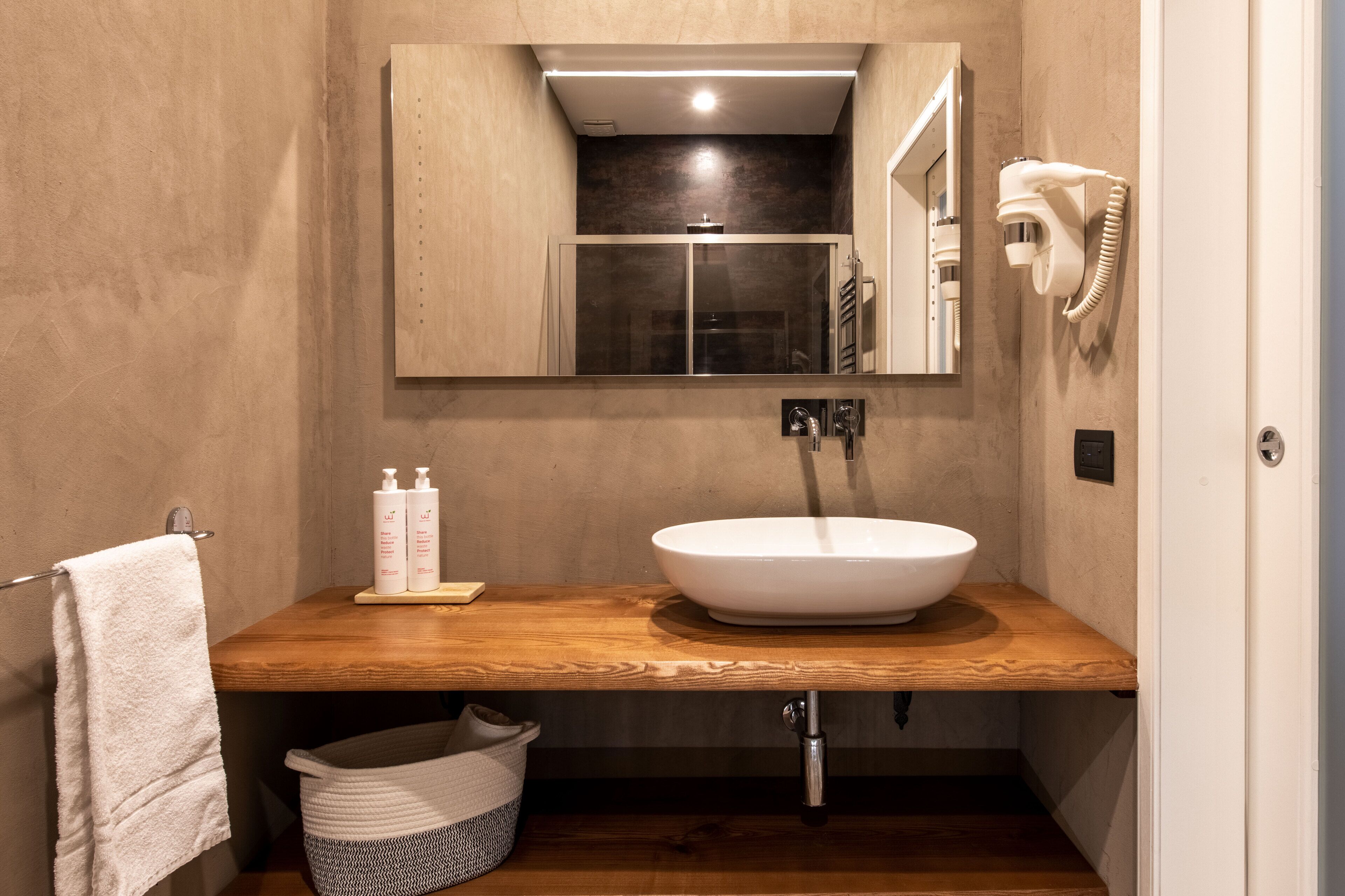 Un baño con tocador de madera, un lavabo blanco, un perchero para toallas, un secador de pelo y un cubo de basura.