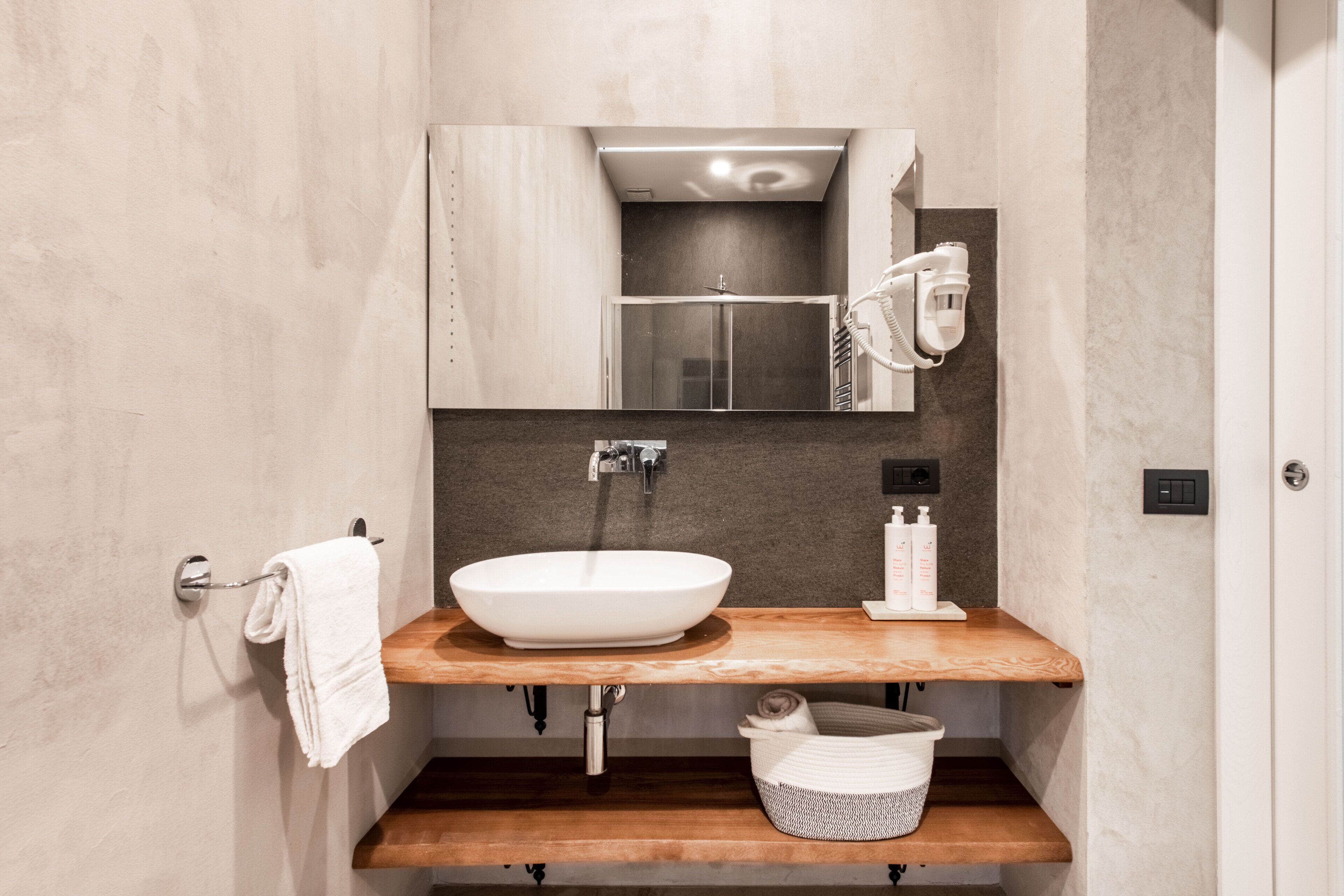 Un baño moderno con tocador de madera, un lavabo blanco, un perchero para toallas y un espejo.