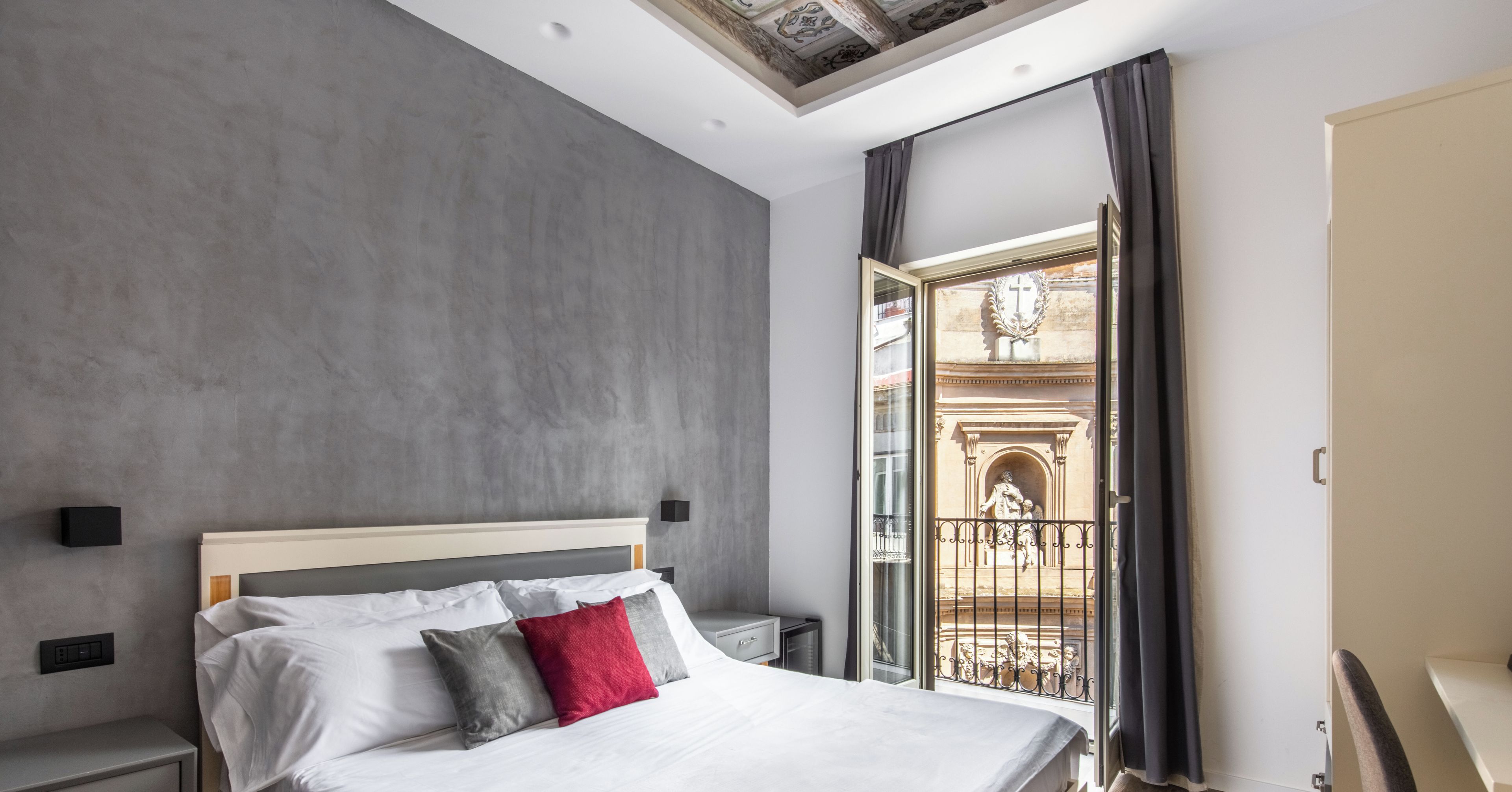 Una camera da letto moderna con un letto grande, una scrivania e un balcone con ringhiera in ferro battuto.