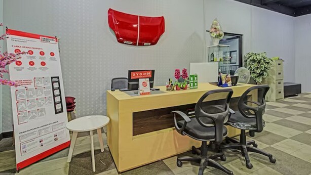 A reception desk with two black office chairs, a small white table, a red and white sign, and a bulletin board with informational posters. - Capital O 3198 Sukomanunggal Inn (Surabaya)