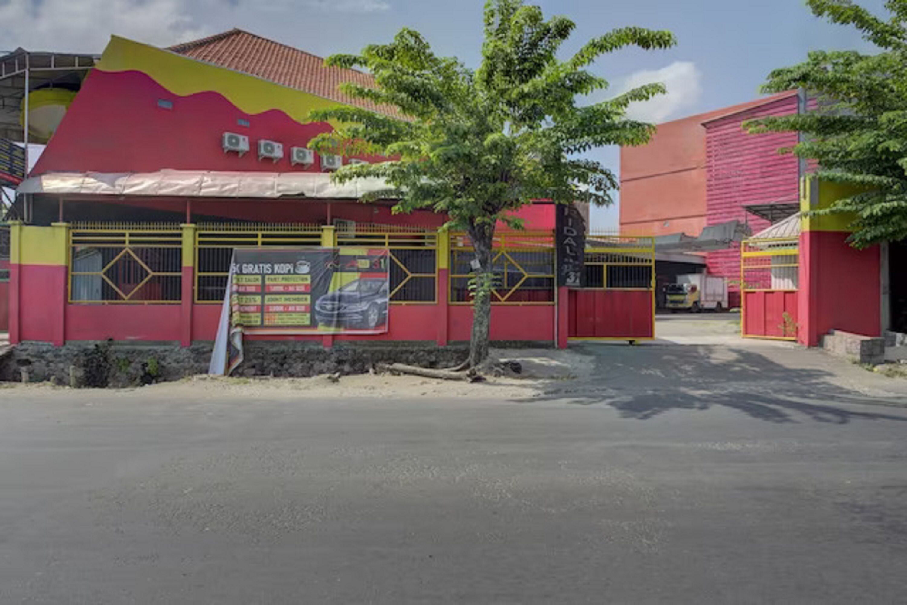 A building with a red and yellow facade, a tree in front, and a signboard.