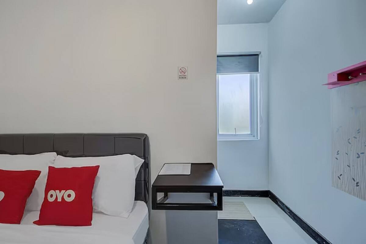 Une chambre d’hôtel avec un lit, deux oreillers rouges, une petite table, une fenêtre et une étagère fixée au mur.