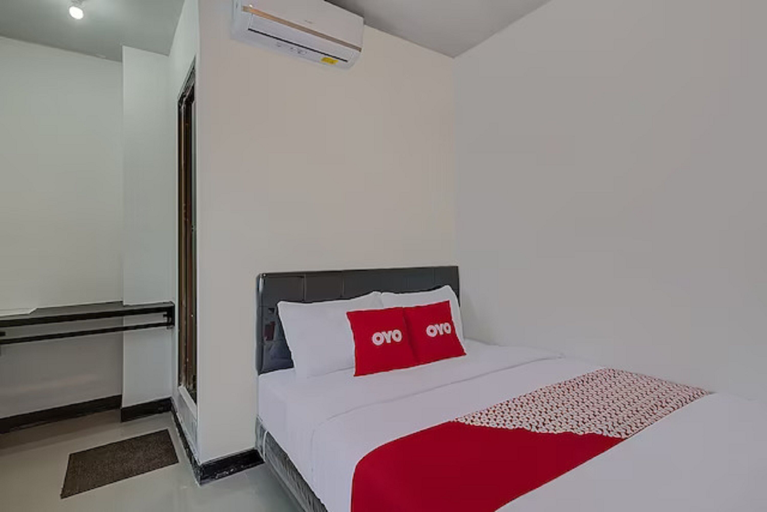 A hotel room with a bed, a red and white bedspread, and a white wall.