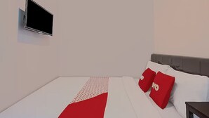 A modern hotel room with a bed, a flat-screen TV mounted on the wall, and red and white pillows. - Capital O 3198 Sukomanunggal Inn (Surabaya)