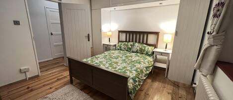 A bedroom with a bed, bedside tables, a nightstand, a radiator, and a door.