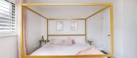 A single bed with a gold frame in a room with white walls, a ceiling fan, and a window with blinds.