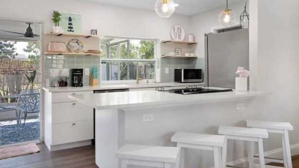 Une cuisine moderne avec des meubles blancs, un îlot central et des luminaires suspendus.