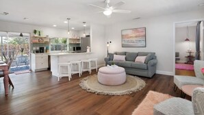 Un salon moderne avec un canapé gris, un pouf rond et un coin repas doté de meubles blancs.