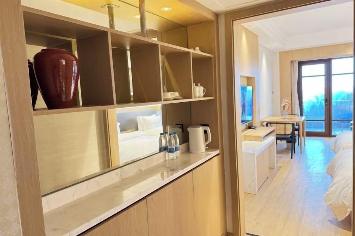 Une chambre d’hôtel équipée d’un lit, d’un bureau, d’une machine à café et d’une étagère où sont disposés des objets décoratifs.