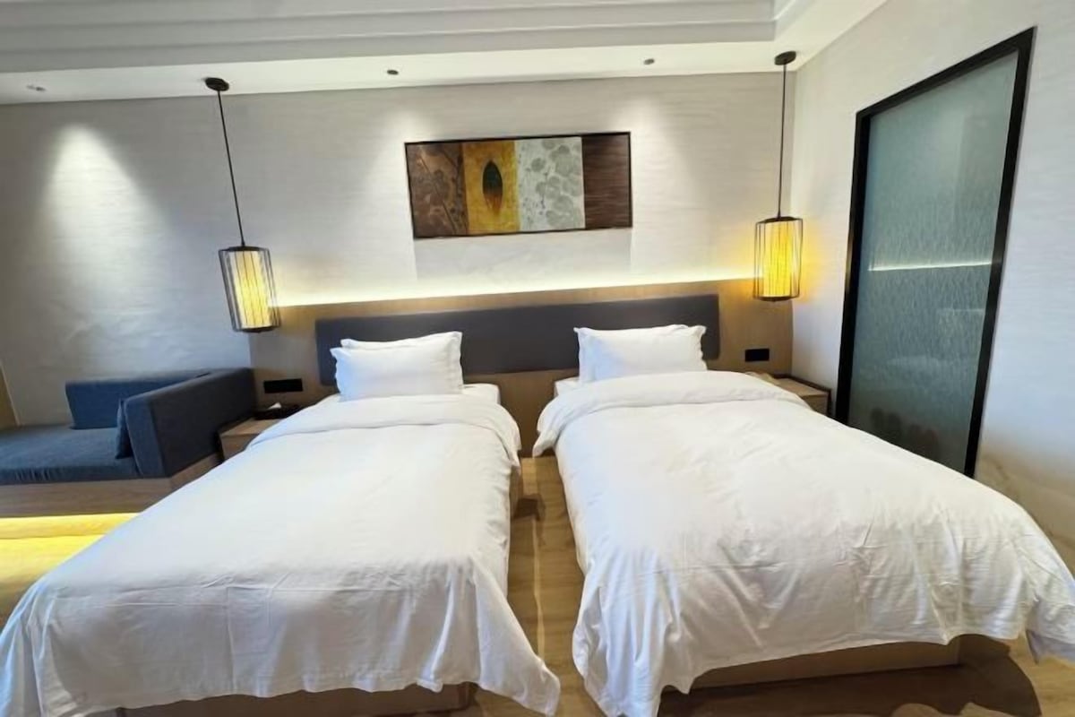 Une chambre d’hôtel avec deux lits simples, un canapé, un tableau au mur et des luminaires suspendus.