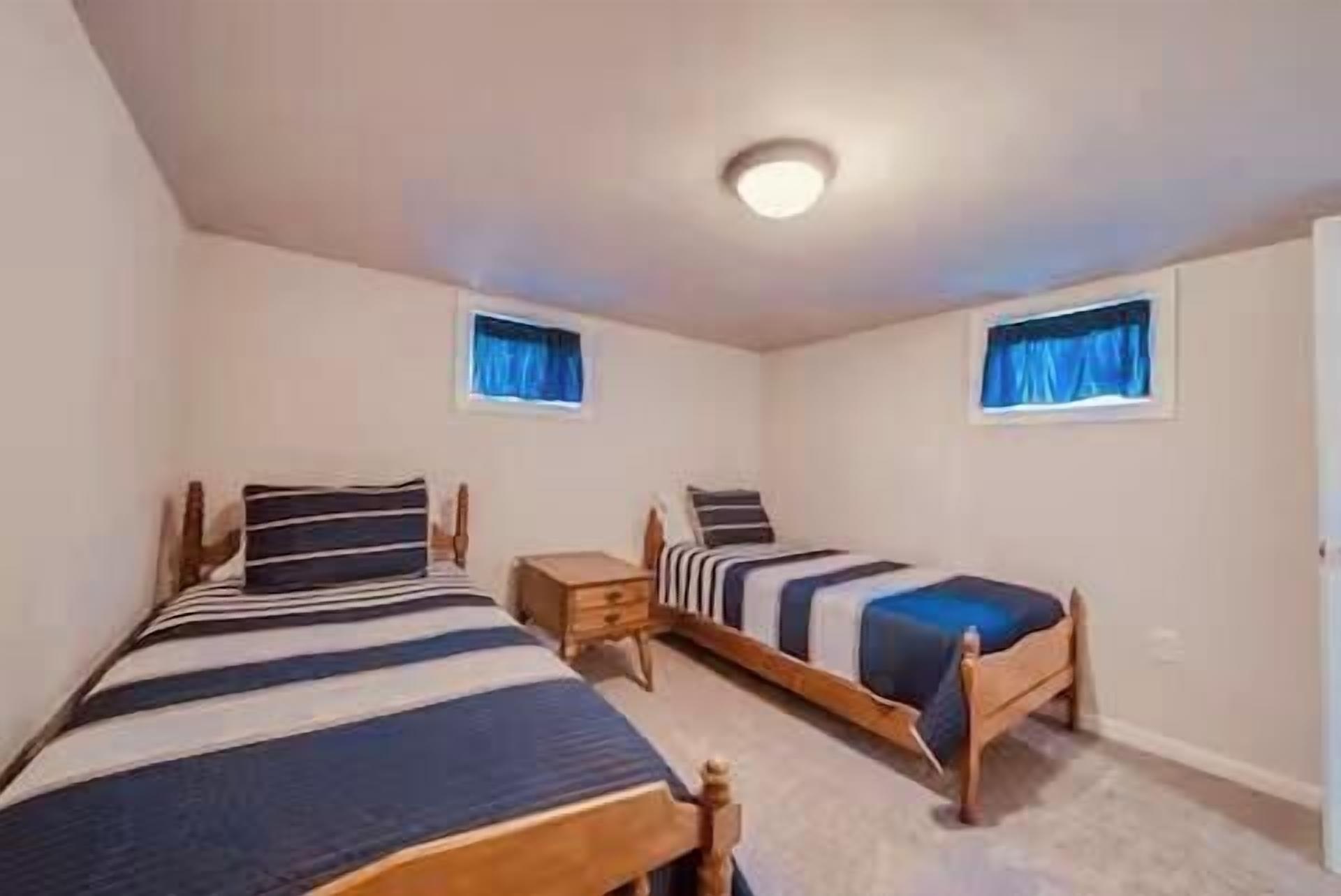 Una habitación con dos camas individuales, una mesita de noche de madera y una lámpara en el techo.