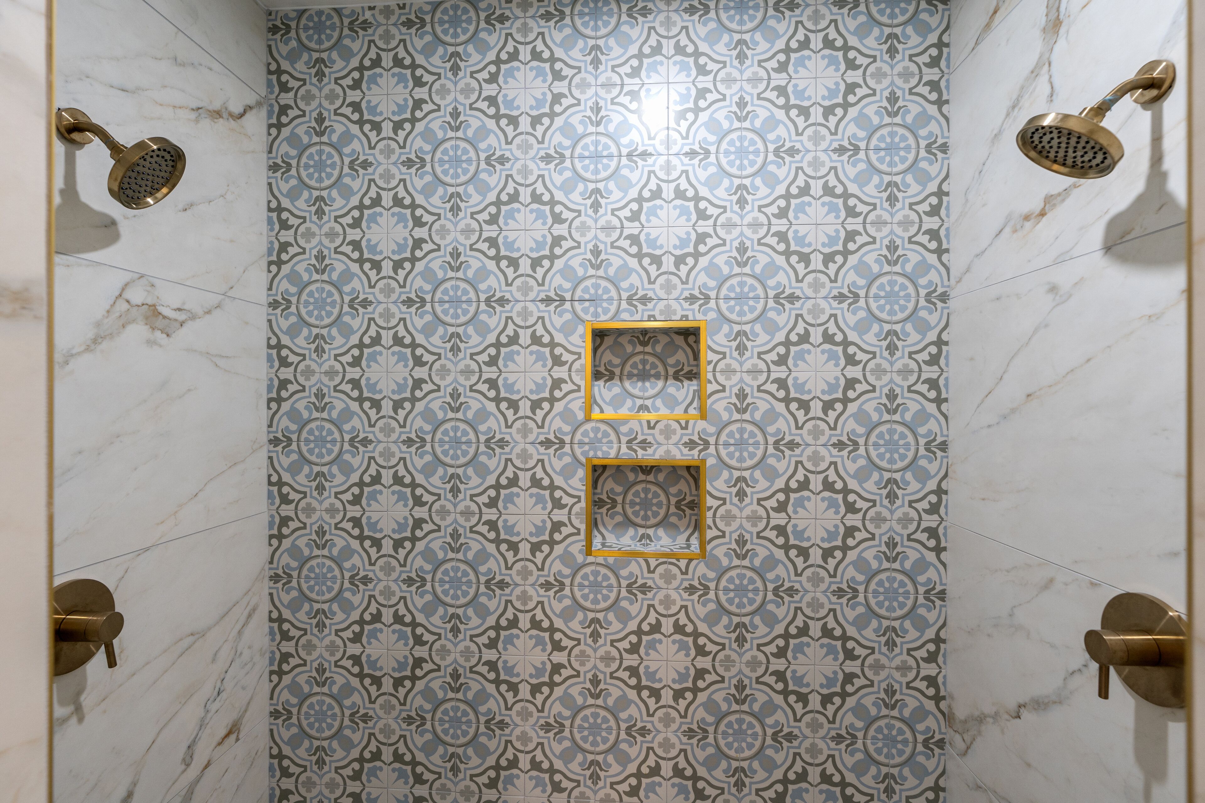 Un baño con baldosas estampadas, dos espejos enmarcados y dos cabezales de ducha.