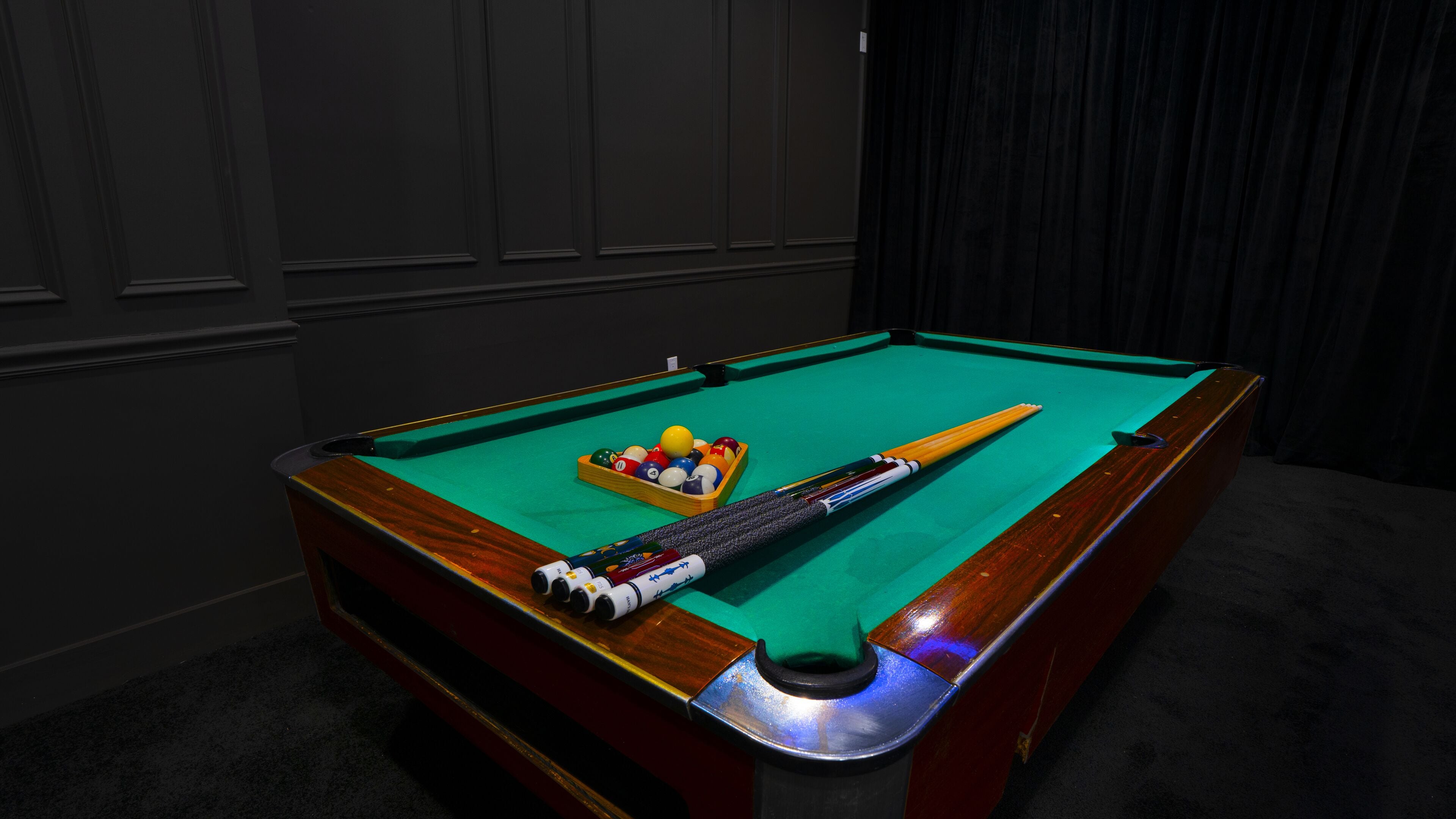A pool table with a cue stick, balls, and a chalk box.
