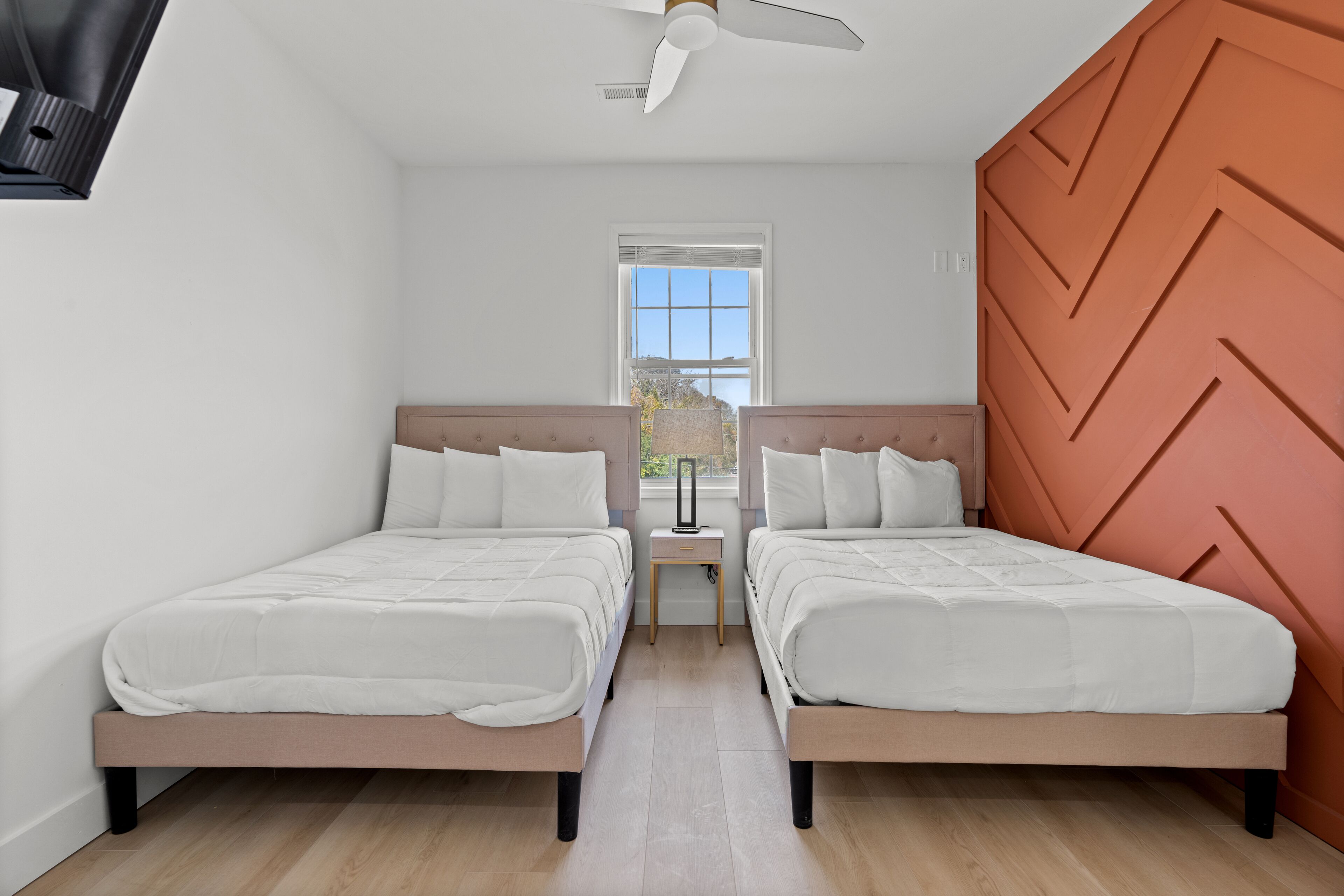 Ein Zimmer mit zwei Betten, einem Deckenventilator, einem Fenster und Blick ins Freie.