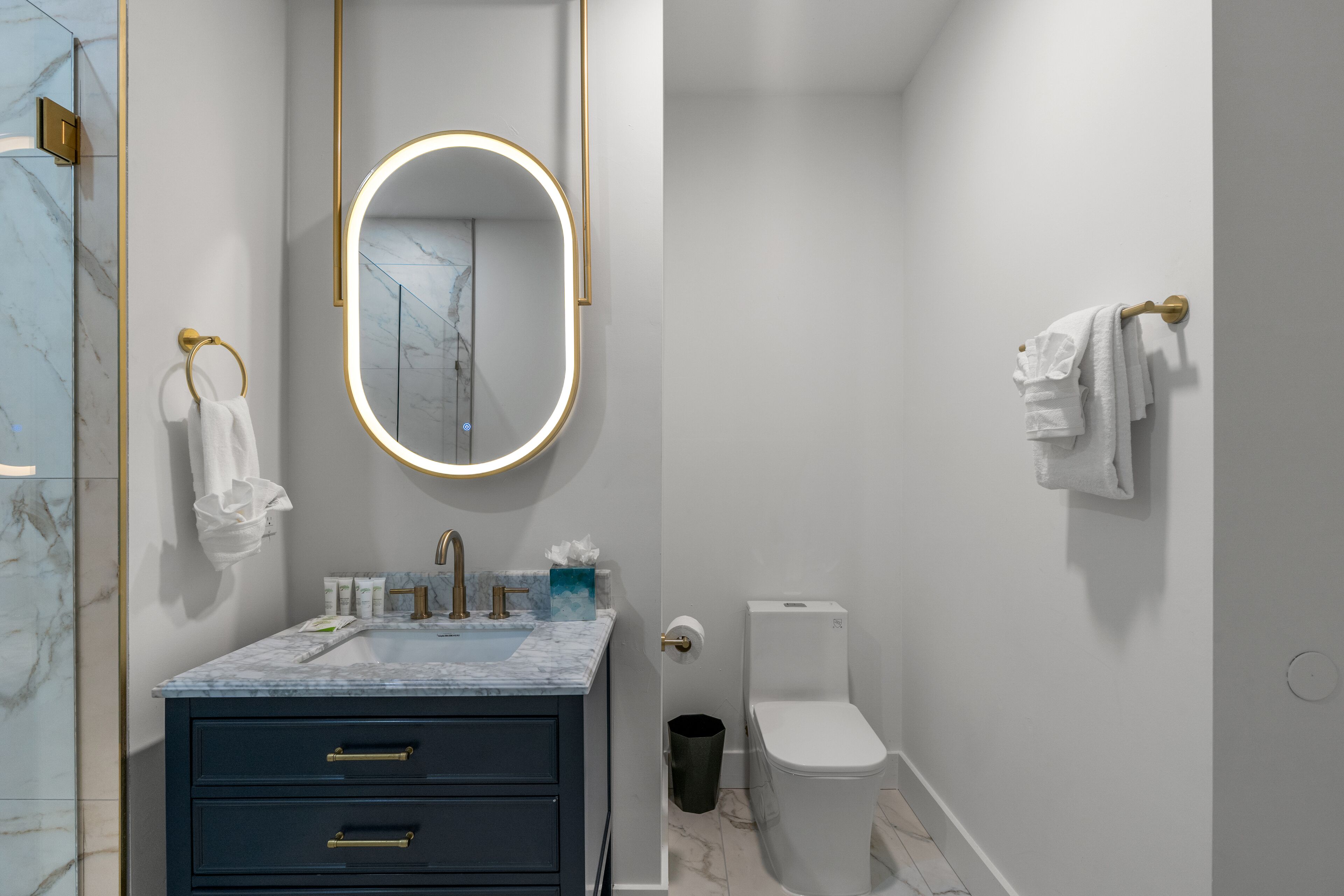 Une salle de bain moderne avec un lavabo en marbre, des toilettes et un miroir avec éclairage intégré.