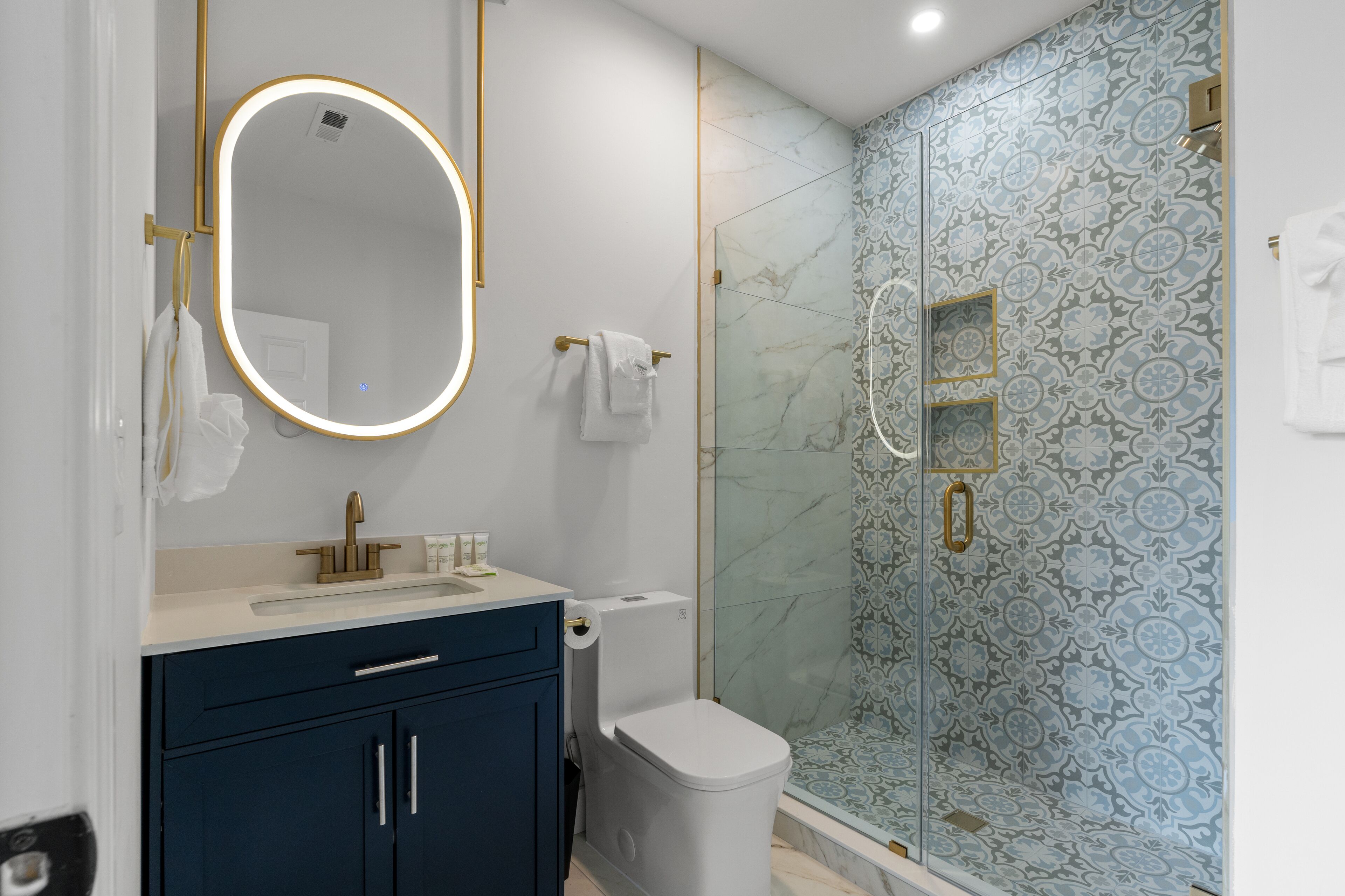 A modern bathroom with a marble shower, a large mirror with a gold frame, and a dark blue vanity.
