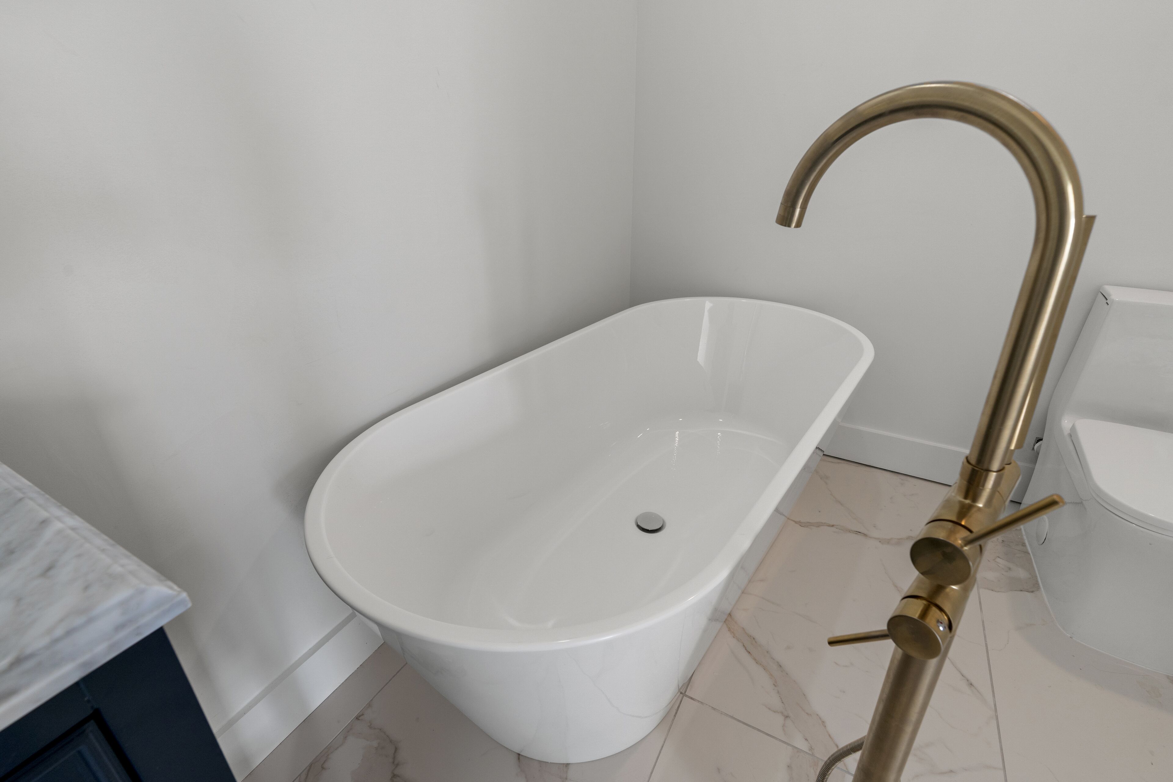 Un baño moderno con una bañera independiente, piso de baldosas de mármol y lavamanos blanco.
