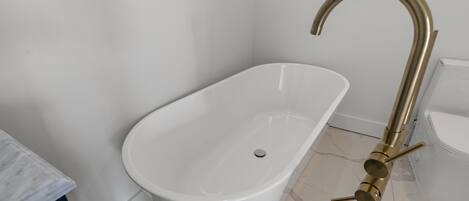Un baño moderno con una bañera independiente, piso de baldosas de mármol y lavamanos blanco.