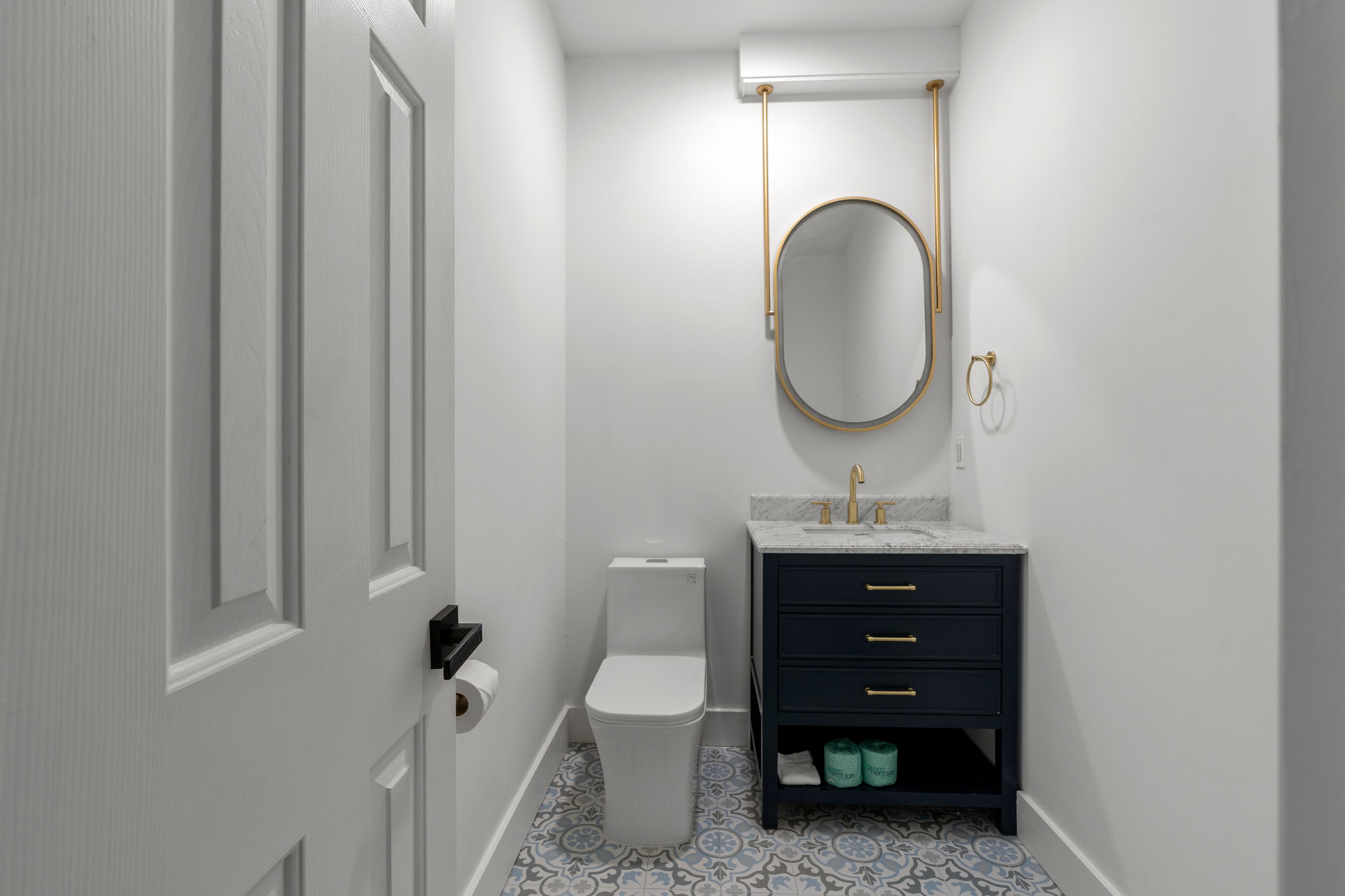 A bathroom with a toilet, a sink with a gold faucet, a dark cabinet with drawers, and a patterned floor.