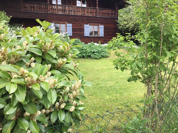Una casa de madera con balcón, rodeada de abundante vegetación y un césped bien cuidado.