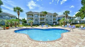 A swimming pool with lounge chairs and a building with balconies in the background. - Quiet Myrtlewood Condo for 4 • Family Fun & Golf Nearby (Myrtle Beach)