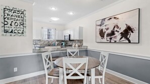 A modern kitchen with white cabinets, a granite countertop, and a dining area with a round table and white chairs. - Quiet Myrtlewood Condo for 4 • Family Fun & Golf Nearby (Myrtle Beach)