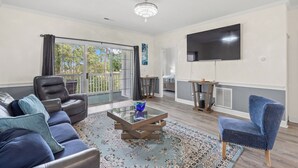 A living room with a sofa, armchair, coffee table, and a TV mounted on the wall. - Quiet Myrtlewood Condo for 4 • Family Fun & Golf Nearby (Myrtle Beach)