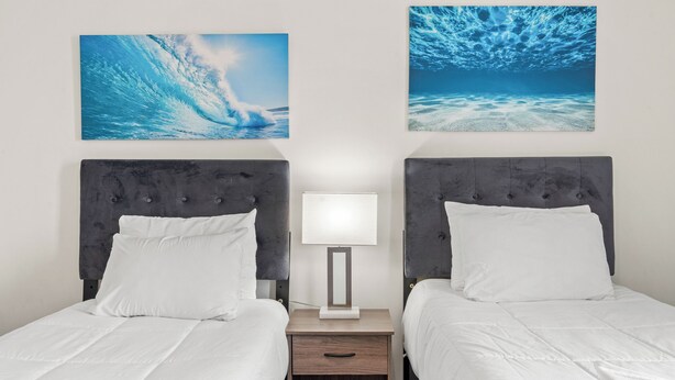 A hotel room with two beds, a nightstand with a lamp, and two wall-mounted artworks depicting underwater scenes. - Quiet Myrtlewood Condo for 4 • Family Fun & Golf Nearby (Myrtle Beach)