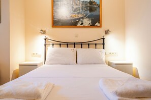 A neatly made bed with white linens, two bedside tables with lamps, and a framed picture of a harbor scene on the wall. - Seaside Luxury Residence near the Airport (Nea Makri)