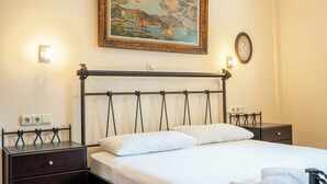 A hotel room with a bed, two bedside tables, a nightstand, a wall-mounted painting, and a wall socket. - Seaside Luxury Residence near the Airport (Nea Makri)