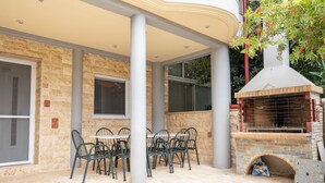 An outdoor patio with a stone wall, a brick barbecue, and a table with chairs. - Seaside Luxury Residence near the Airport (Nea Makri)