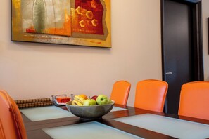 A dining table with a fruit bowl, orange chairs, and a painting on the wall. - Seaside Luxury Residence near the Airport (Nea Makri)