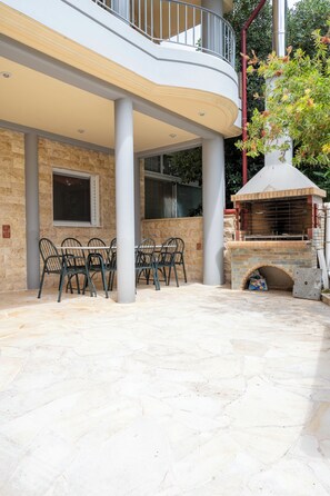 A patio area with a round table and chairs, a brick oven, and a balcony with a railing. - Seaside Luxury Residence near the Airport (Nea Makri)