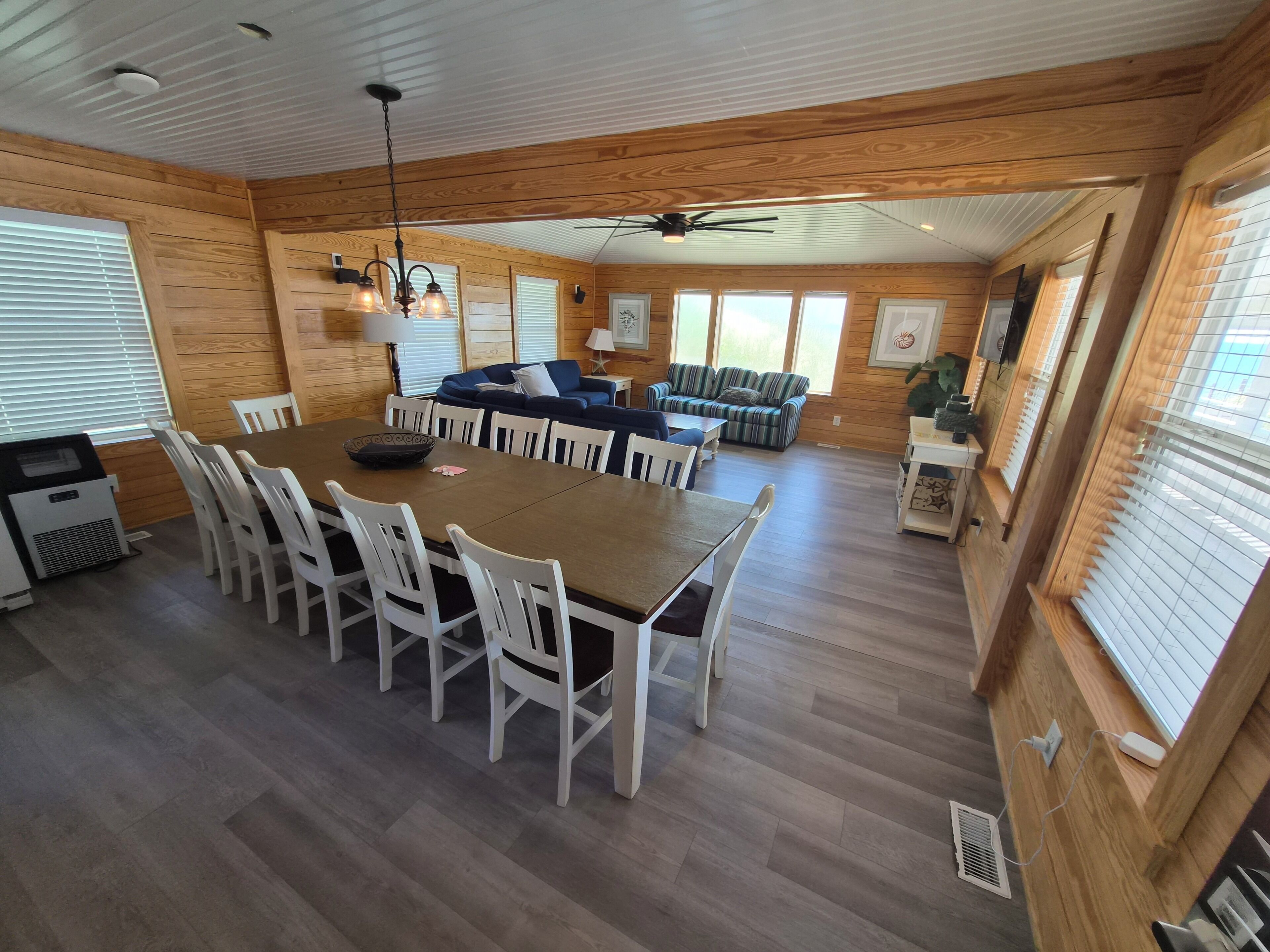 A wooden interior with a dining table, chairs, a sofa, and a ceiling fan.