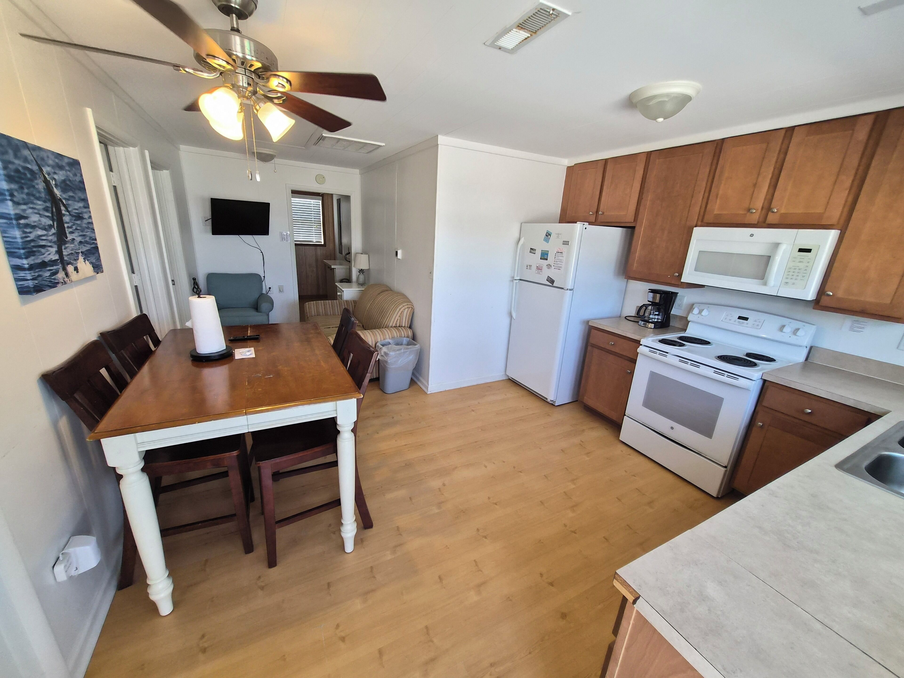 A kitchen with wooden cabinets, a refrigerator, a microwave, an oven, and a dining area with a table and chairs.