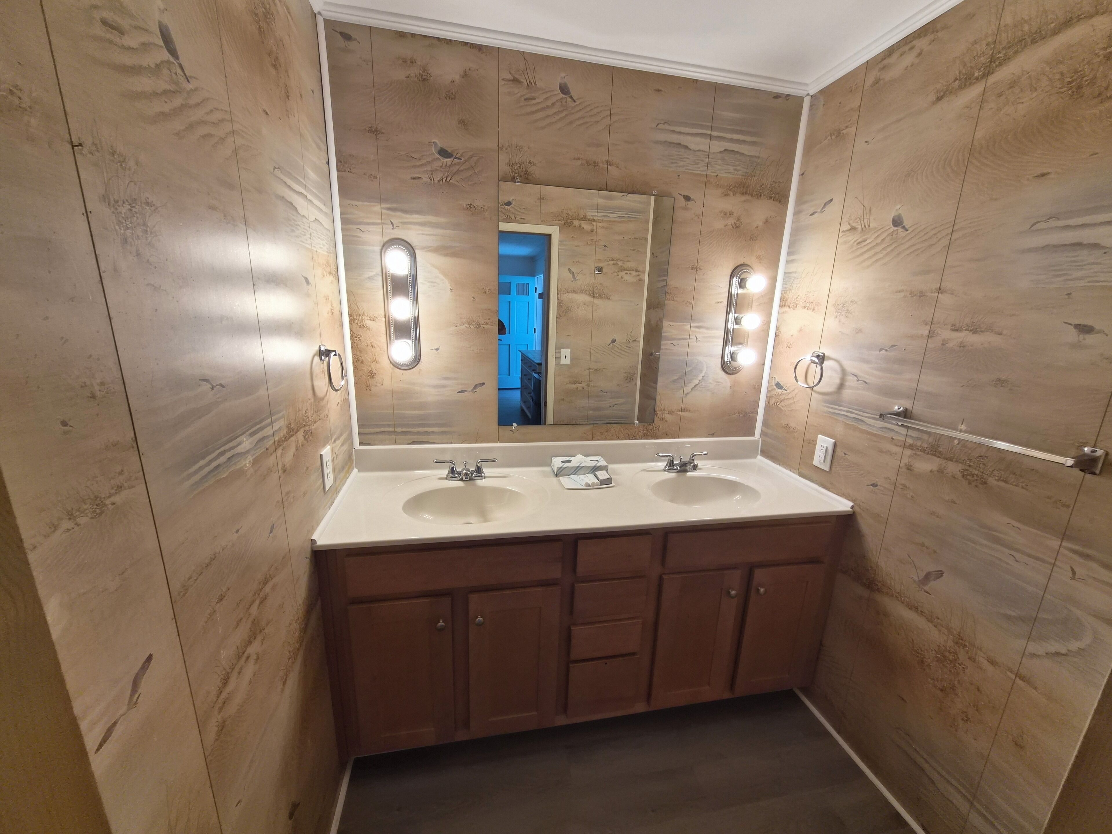 Une salle de bain avec des murs recouverts de panneaux en bois, deux lavabos et un grand miroir avec éclairage.