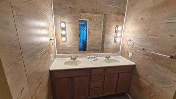 Une salle de bain avec des murs recouverts de panneaux en bois, deux lavabos et un grand miroir avec éclairage.