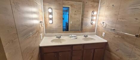 A bathroom with wooden panel walls, two sinks, and a large mirror with lights.
