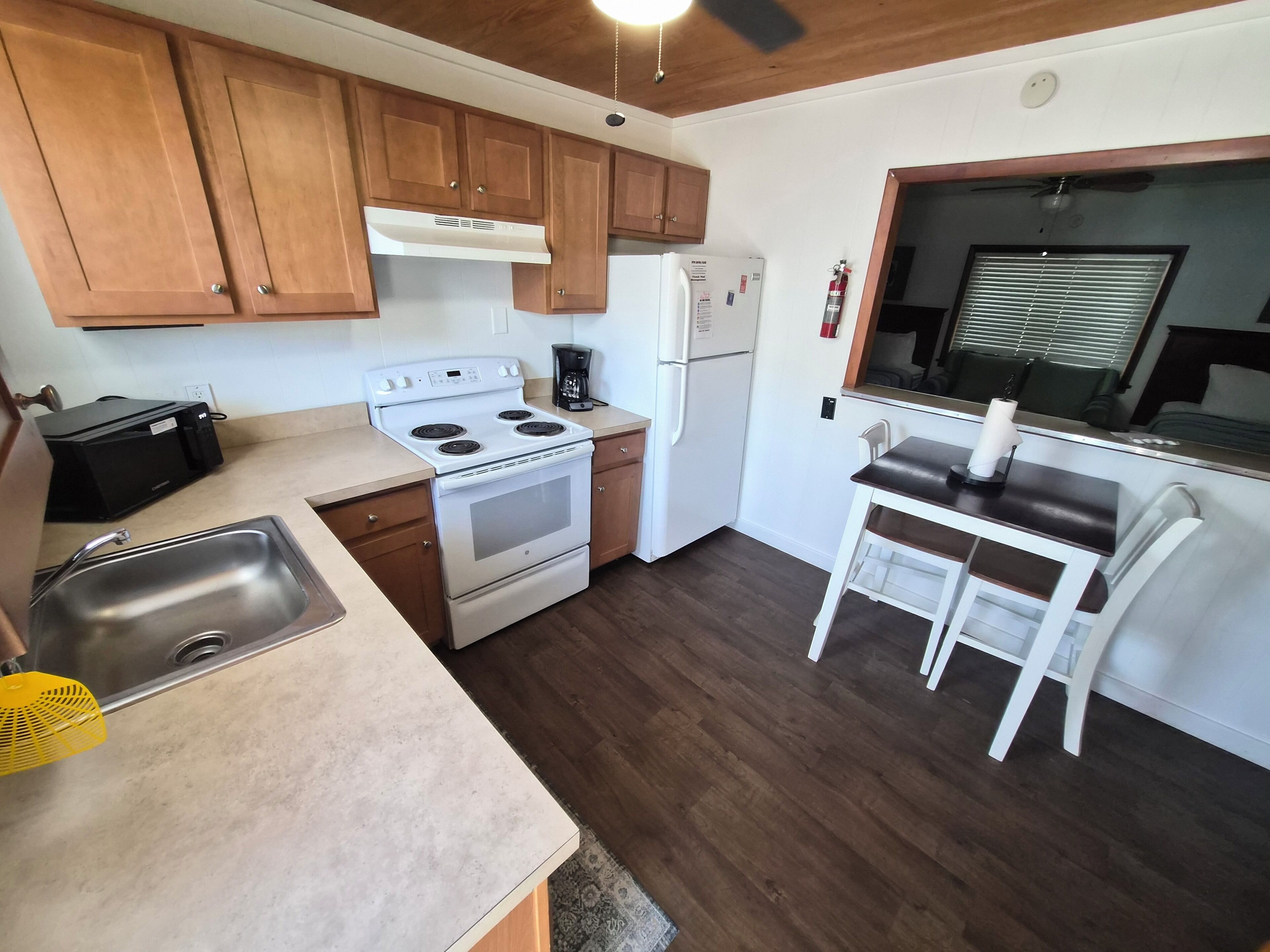 A compact kitchen with wooden cabinets, a white stove, a refrigerator, and a small dining area with a table and chairs.