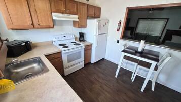 A compact kitchen with wooden cabinets, a white stove, a refrigerator, and a small dining area with a table and chairs.
