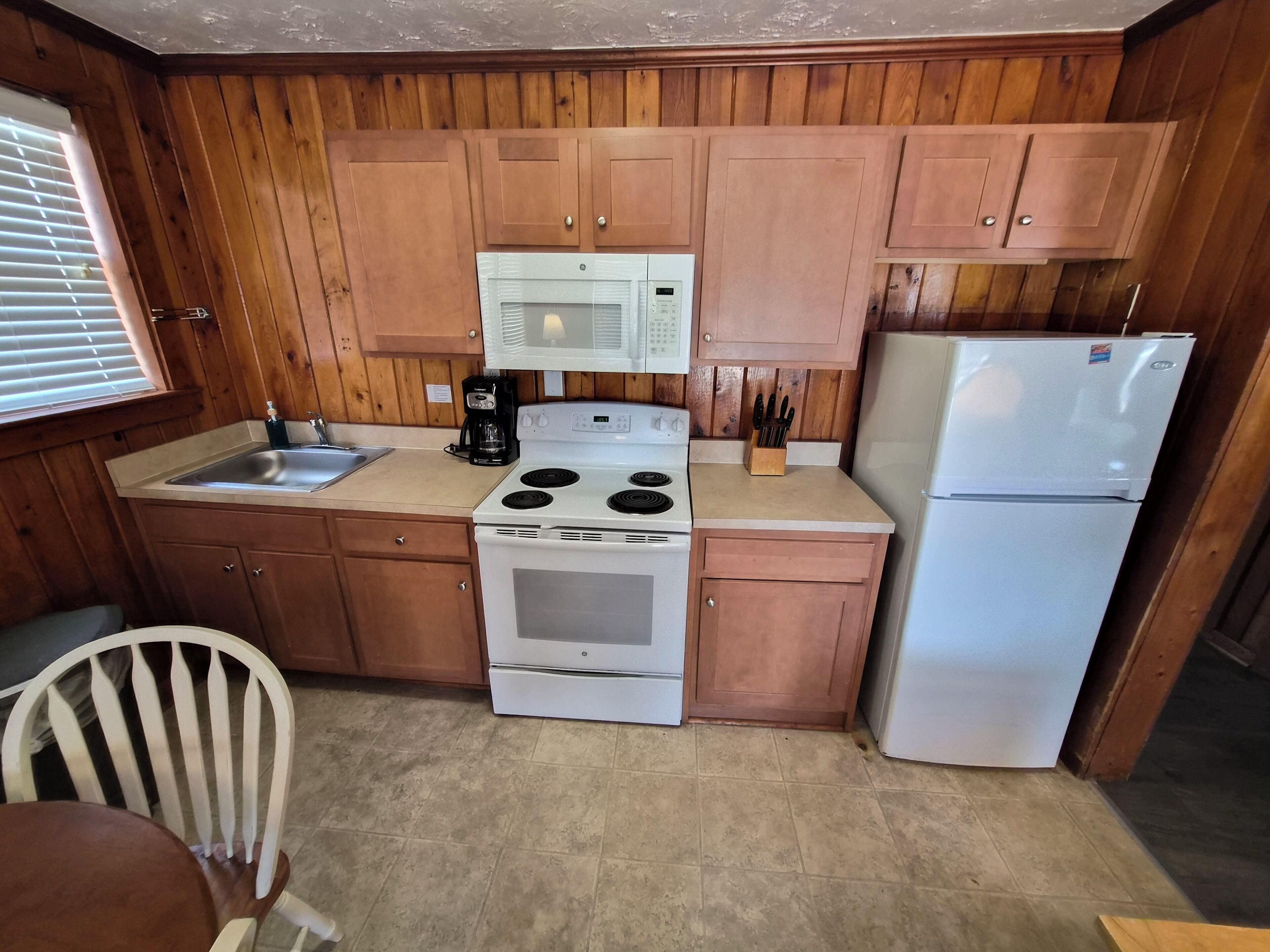 Une cuisine de taille réduite, dotée de meubles en bois, d’un four à micro-ondes, d’une cuisinière, d’un évier et d’un réfrigérateur.