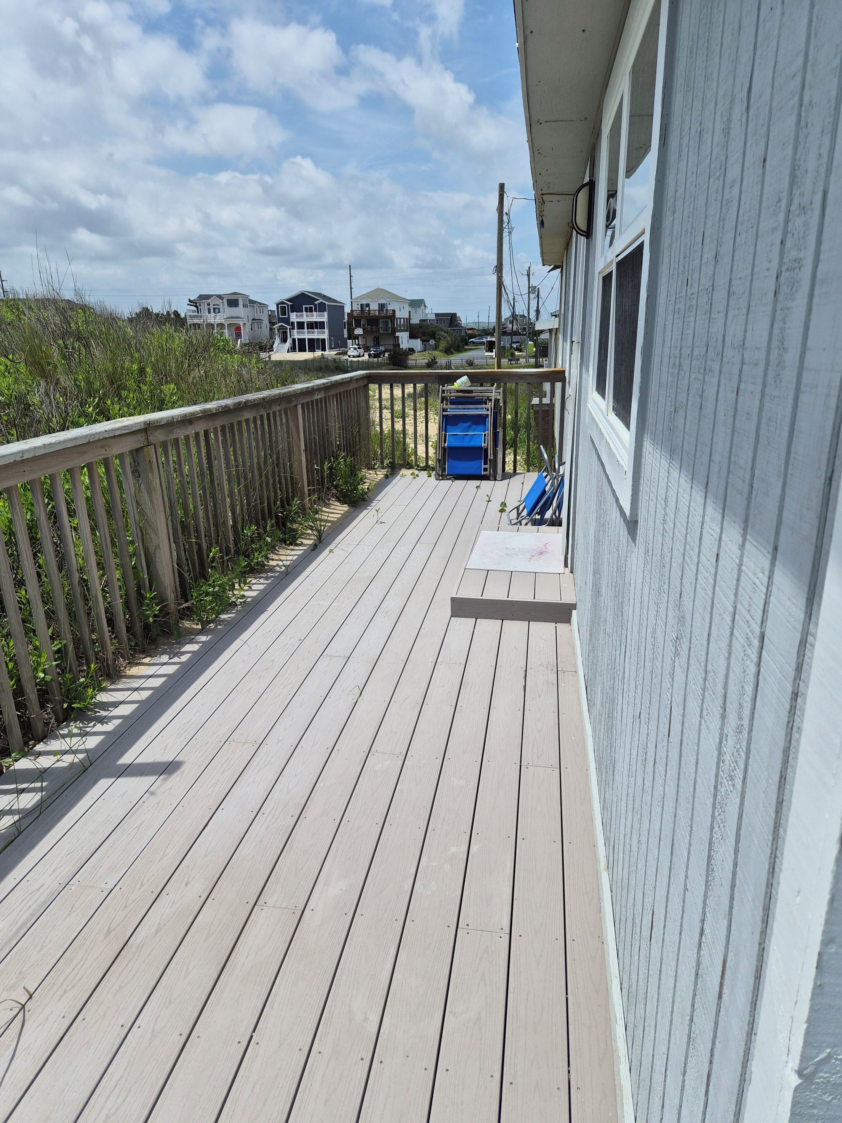 A wooden deck with a railing, a blue trash bin, and a window.
